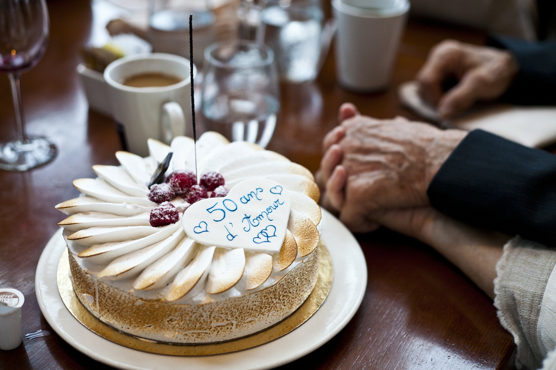 A couple celebrating their golden anniversary, holding hands next to a table with a cake adorned with sparklers. The image captures a joyful moment of love and celebration